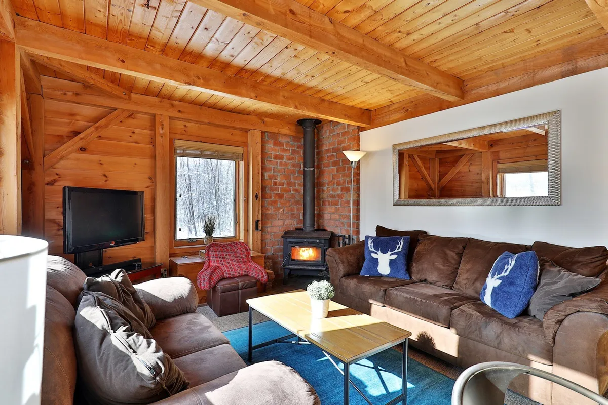 The hero image showcases a cozy, wood-beamed interior with a brick fireplace as the focal point. Plush sofas with decorative pillows invite relaxation, while natural light filters through, creating a warm, inviting atmosphere perfect for gathering with family and friends.