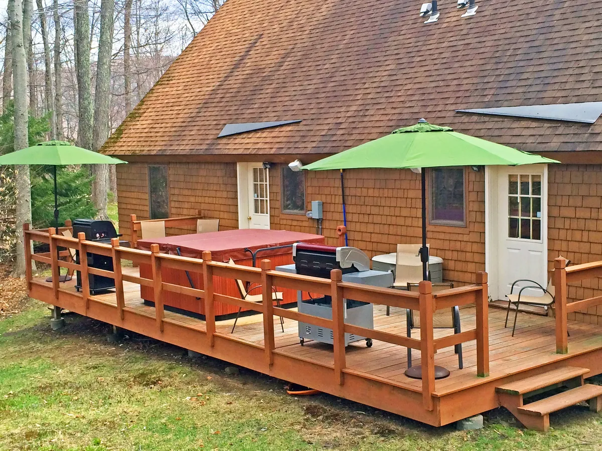 An inviting exterior setup with a hot tub, grill, patio seating, and green umbrellas—perfect for relaxing after a day of adventure or gathering for a meal outdoors. Surrounded by greenery, it feels both private and connected to nature.