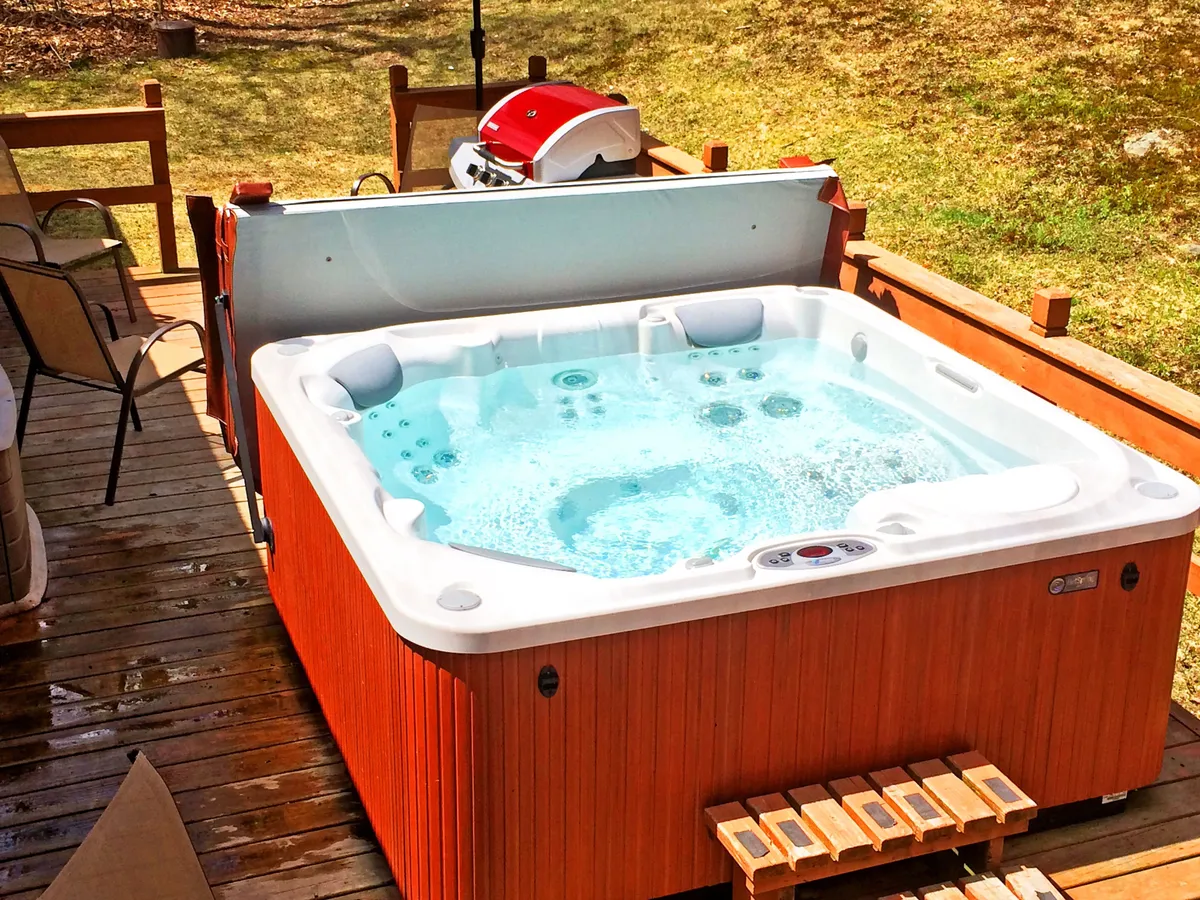 This exterior image features a hot tub and BBQ grill on a wooden deck, with outdoor seating and lush greenery in the background. The area is inviting, suggesting relaxation after a day of adventure and spaces to unwind or gather for meals.