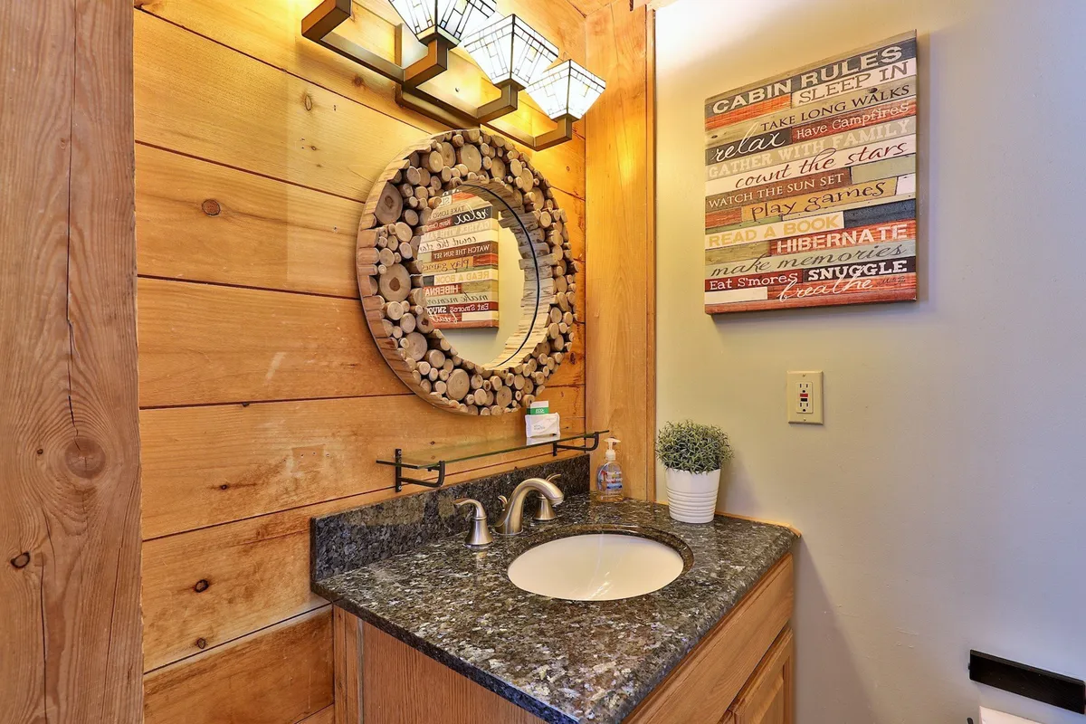 An inviting interior scene with a granite countertop, circular mirror, and wooden accent wall. Decorative lighting and a 'cabin rules' sign create a welcoming, homey atmosphere. The area is suitable for preparing for the day’s activities or relaxing in the evening.
